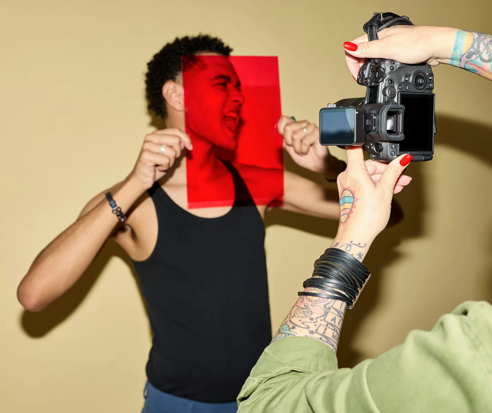 Fotografka robi zdjęcie mężczyźnie, który trzyma przed twarzą przezroczystą czerwoną folię.
